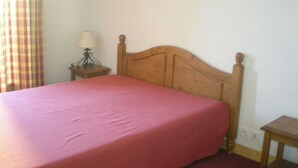 A single bed with a wooden headboard in a room with a plain wall and a small bedside table with a lamp. - Apartment in Le Village with Balcony (Notre Dame de Bellecombe)