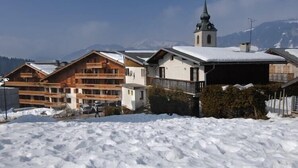 A snow-covered building with a church steeple in the background. - Apartment in Le Village with Balcony (Notre Dame de Bellecombe)