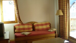 A small room with a single bed, a table, a lamp, and a window with curtains. - Apartment in Le Village with Balcony (Notre Dame de Bellecombe)