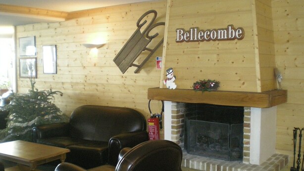 A cozy room with a fireplace, a wooden wall with a sign reading 'Bellecombe,' and a Christmas tree. - Apartment in Le Village with Balcony (Notre Dame de Bellecombe)
