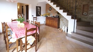 Un comedor con una mesa lista para cuatro personas, una escalera y una zona de cocina con pared de piedra.