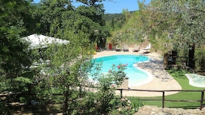 Una piscina rodeada por una valla de madera, con una carpa blanca y sillones de descanso al fondo.