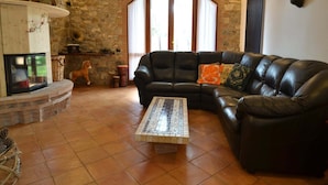 Una sala de estar con pared de piedra, chimenea, sofá de cuero negro y suelo de baldosas.