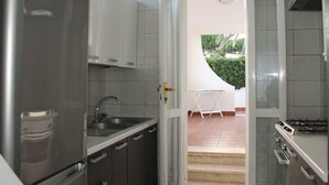 A modern kitchen with grey tiles, stainless steel appliances, and a view of a patio with a table and chairs.