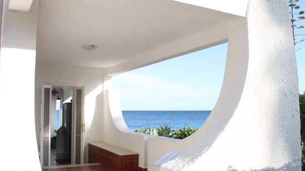 A balcony with a view of the sea, white walls, and a tiled floor.