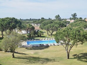 Un espace piscine doté de chaises longues et d’une piscine à l’eau d’un bleu limpide, entouré d’arbres et offrant une vue sur un quartier résidentiel.