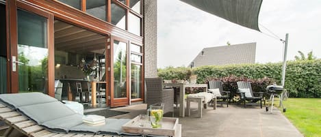 Un patio con un banco de madera, una mesa con sillas y una parrilla.