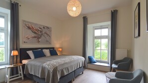 Ein Schlafzimmer mit Bett, Nachttischlampen, einer Sitzgelegenheit an einem Fenster und einem großen abstrakten Gemälde an der Wand.