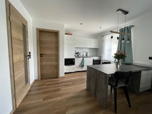 Una cocina moderna con armarios blancos, una puerta de madera y un comedor con mesa y sillas.