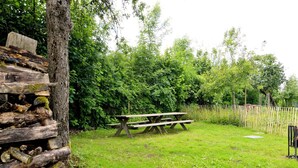 A picnic table in a grassy area with a wooden fence and trees in the background.