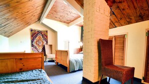 A bedroom with a sloped ceiling, a bed, a chair, a window, and a wall with a patterned tapestry.