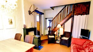 A cozy living room with a wooden dining table, two armchairs, a sofa, a staircase, and a mounted deer head.