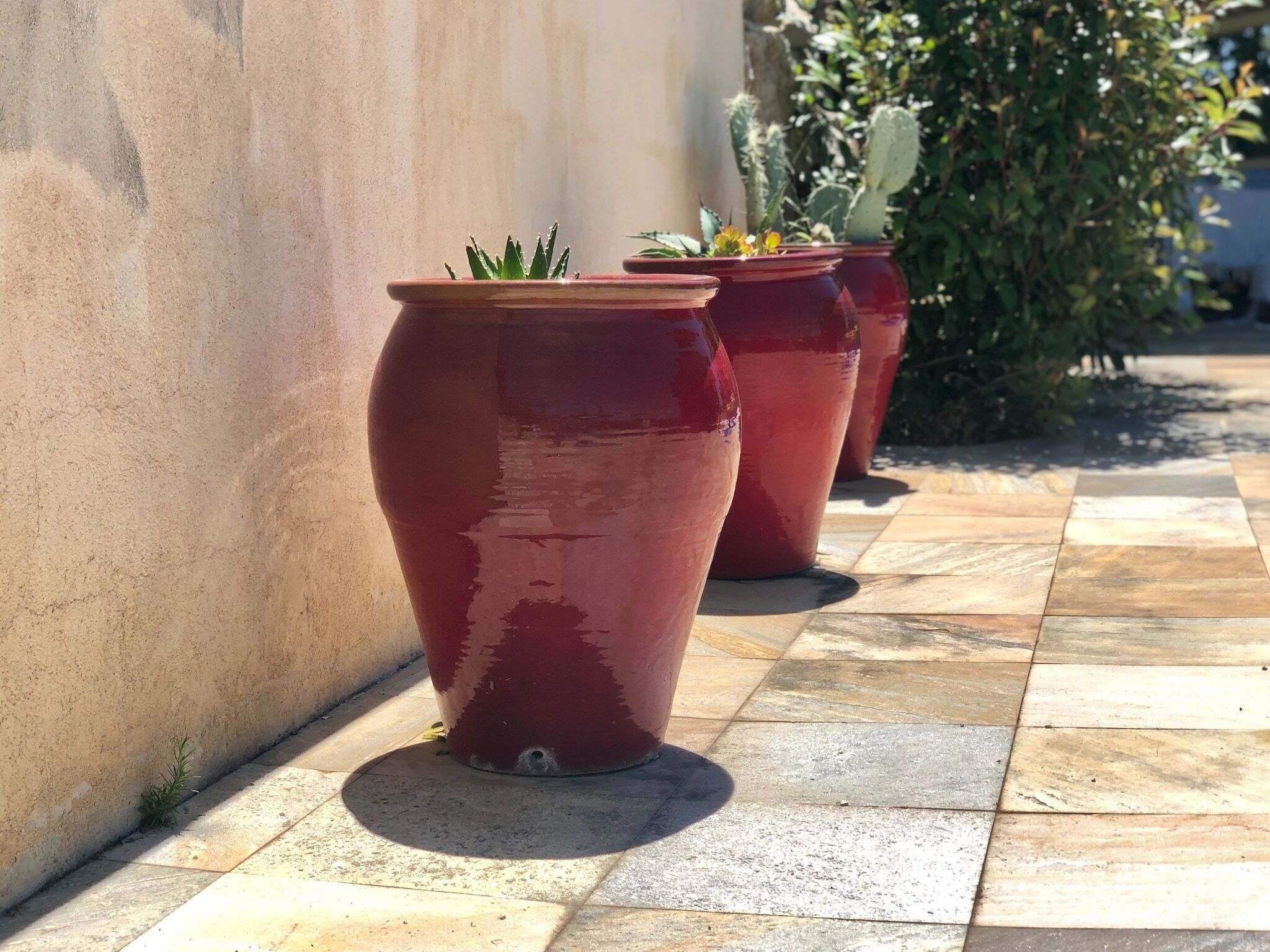 Three large red pots on a tiled patio.
