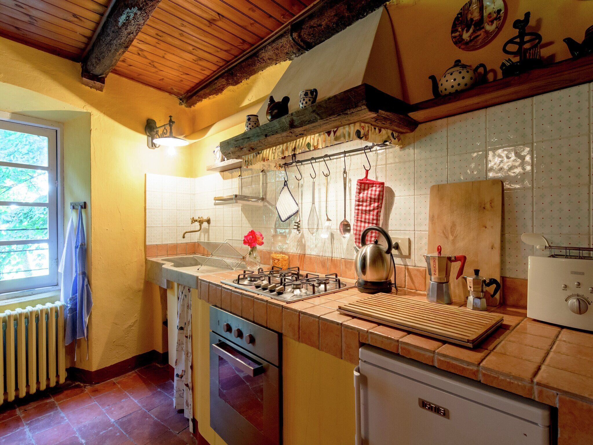 A kitchen with a gas stove, oven, and refrigerator. There is a window with a view of greenery outside.