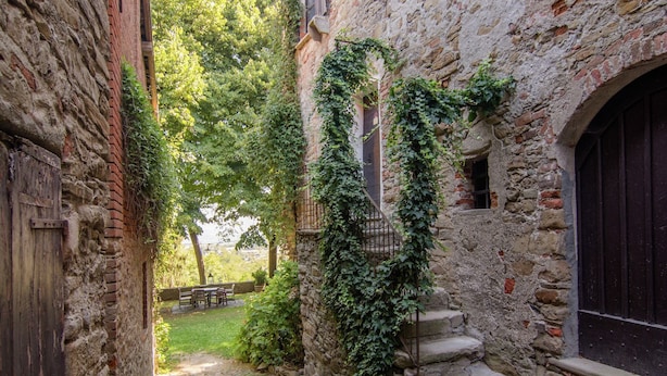Une ruelle étroite pavée de pierres, bordée de murs en pierre, avec une porte en bois et un escalier menant à un niveau supérieur.