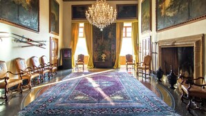 Une vaste pièce agrémentée d’un grand lustre décoratif, d’un long tapis à motifs et de plusieurs chaises en bois disposées autour d’une table centrale.