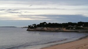 A coastal landscape with a sandy beach, calm sea, and a rocky cliff with vegetation. - Coastal Getaway with Pool (Fouras)