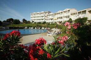 Ein Hotel mit Pool, Liegestühlen und einem Garten mit roten Blumen.
