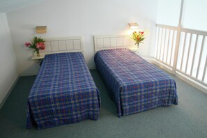 A room with two single beds, each with a headboard and a bedside table with a lamp.