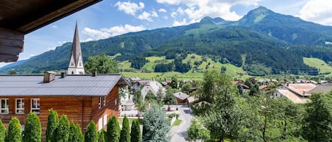 A wooden building with a church steeple, surrounded by green hills and a clear sky.