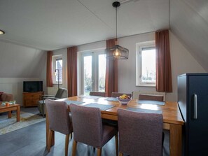 Ein Essbereich mit einem Holztisch, vier Stühlen, einer Obstschale und einem Fernseher auf einem Schrank.