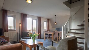 A modern living room with a sofa, a coffee table, and a dining area with chairs. There is a staircase leading to an upper floor.
