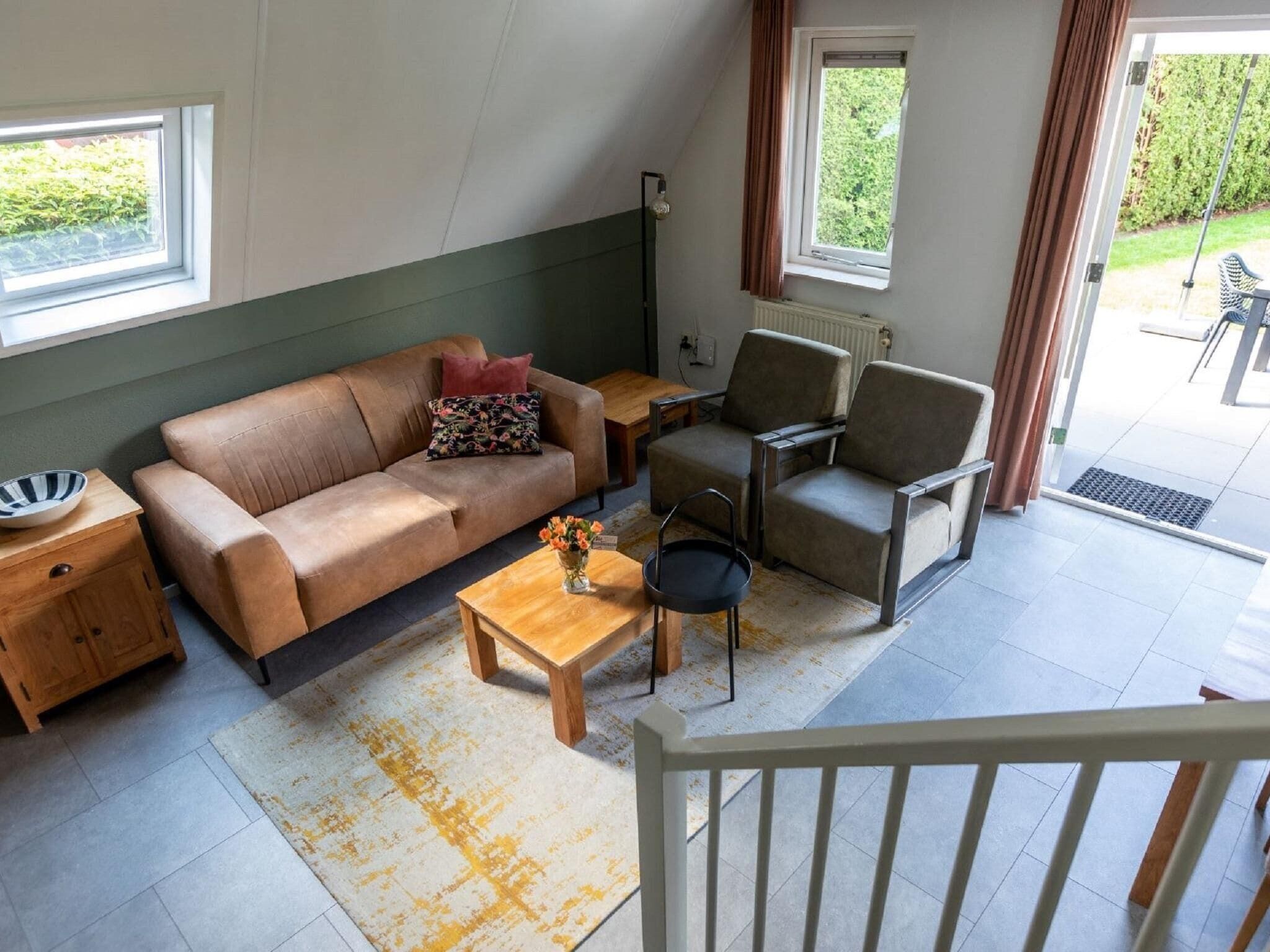 Un salon comprenant un canapé, deux fauteuils, une table basse et une petite table sur laquelle se trouve un bol. Il y a des fenêtres et une vue sur l’extérieur.