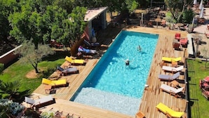 Une piscine rectangulaire dotée d’une terrasse en bois, entourée de chaises longues et de parasols, située dans un cadre verdoyant et luxuriant.