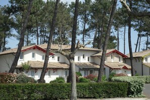 A row of white buildings with red accents, surrounded by trees and greenery.