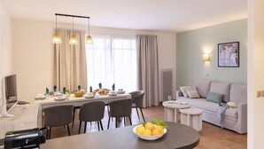A modern living room with a dining area, a sofa, a coffee table, and a TV. - Villa in France by Golf Course with Pool (Gujan Mestras)