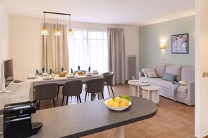 Uma sala de estar moderna com área de jantar, sofá, mesa de centro e televisão.