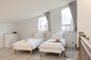 A bedroom with two beds, a dresser, and a window with curtains.