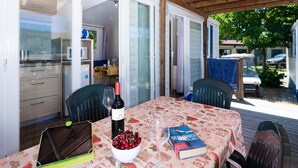 Un espacio de comedor al aire libre con una mesa dispuesta para dos personas, una botella de vino, un bol de cerezas y un libro.