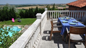 A terrace with a table set for dining, overlooking a pool and countryside.