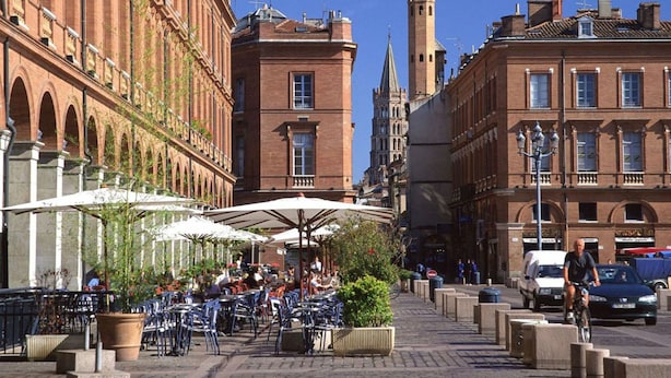 A street with outdoor seating, red brick buildings, and a tower in the background.