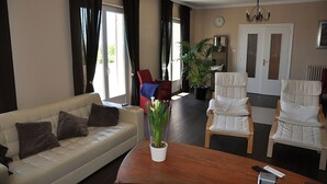 A living room with a sofa, chairs, a wooden coffee table, a potted plant, and a clock on the wall.