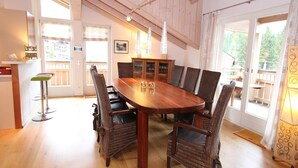 Spiseområde med et træbord og fletstole, et skab med glasdøre, samt udsigt gennem store vinduer.