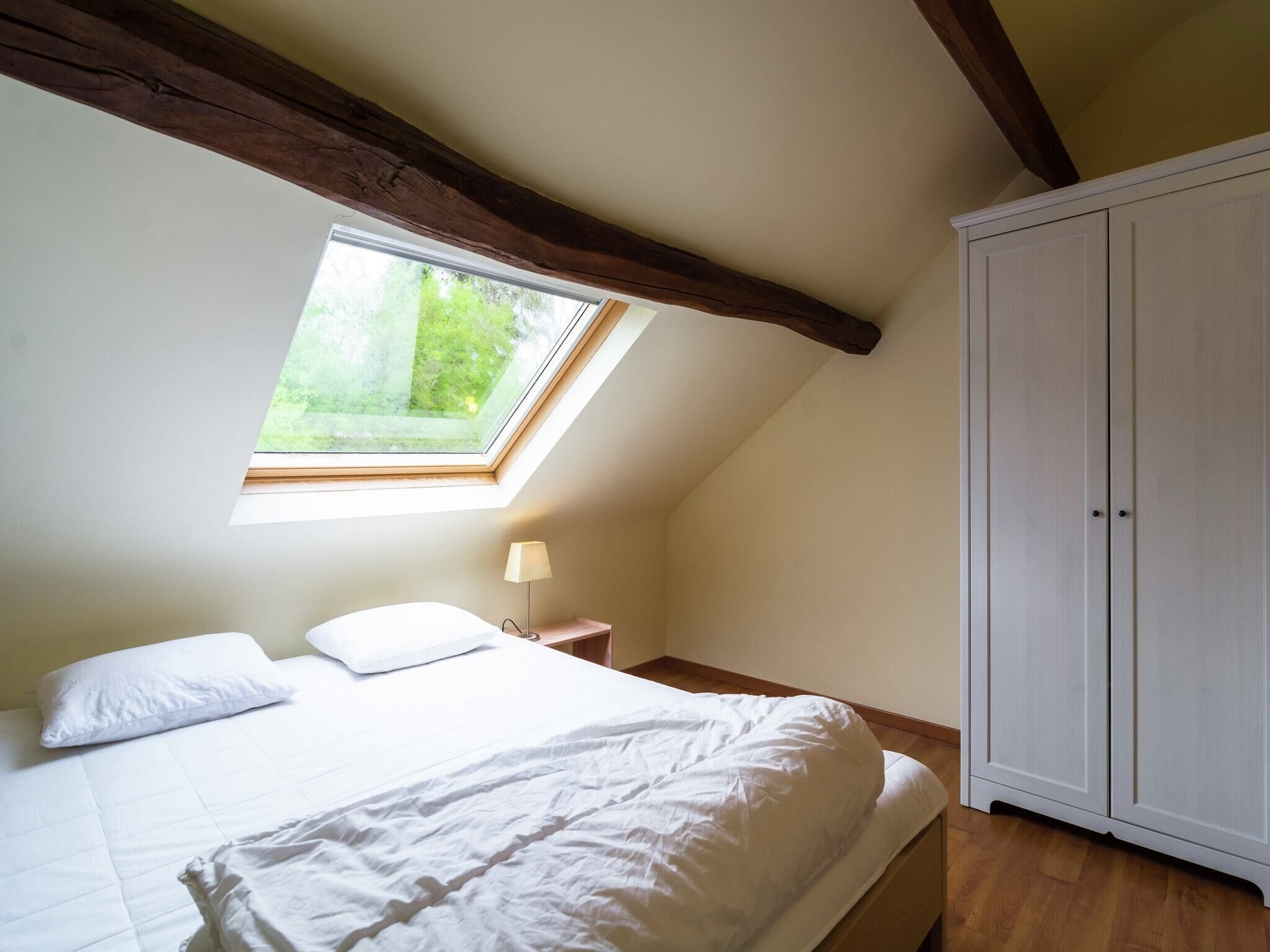 A bedroom with a skylight, a bed, a nightstand, and a wardrobe.