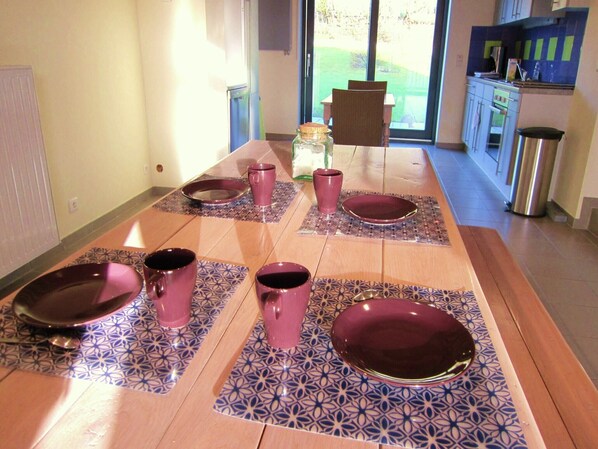 A dining area with a long table set for four, featuring patterned placemats and matching tableware.
