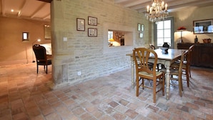 A rustic dining area with exposed stone walls, a wooden dining table, and chairs. There is a chandelier hanging from the ceiling and a window providing natural light. - Manor in Normandy with Spa and Pool (Lantheuil)