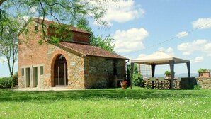 Ein rustikales Steinhaus mit Ziegeldach, einem Rundbogenportal und einem kleinen Garten mit einem Gazebo.