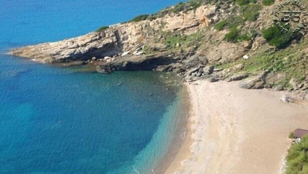 Eine Küstenlandschaft mit blauem Meer, Sandstrand und Felsen.