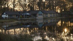 Un bâtiment situé au bord du lac, doté d’un quai, entouré d’arbres et illuminé par le coucher du soleil.