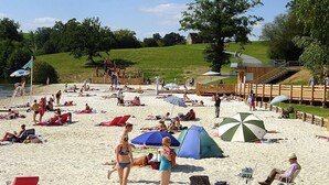 A beach with people sunbathing, tents, and a wooden structure. - Chalet in picturesque medieval village (Segur-Le-Chateau)