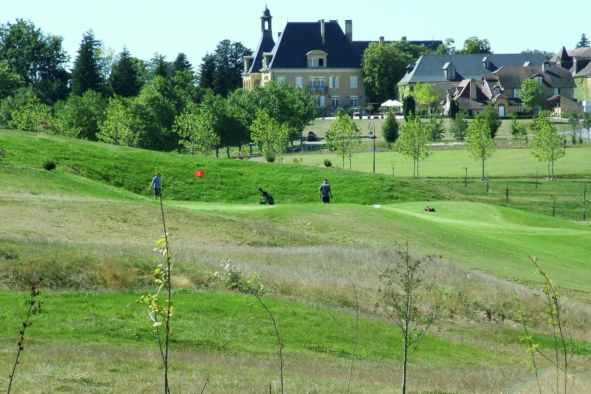Een golfbaan met een groot huis op de achtergrond.