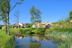Une propriété paisible située au bord d’un lac, avec un étang, des bâtiments en pierre et une végétation luxuriante.