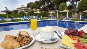 Frühstücksecke mit Croissants, Obst und einem Glas Orangensaft am Pool.