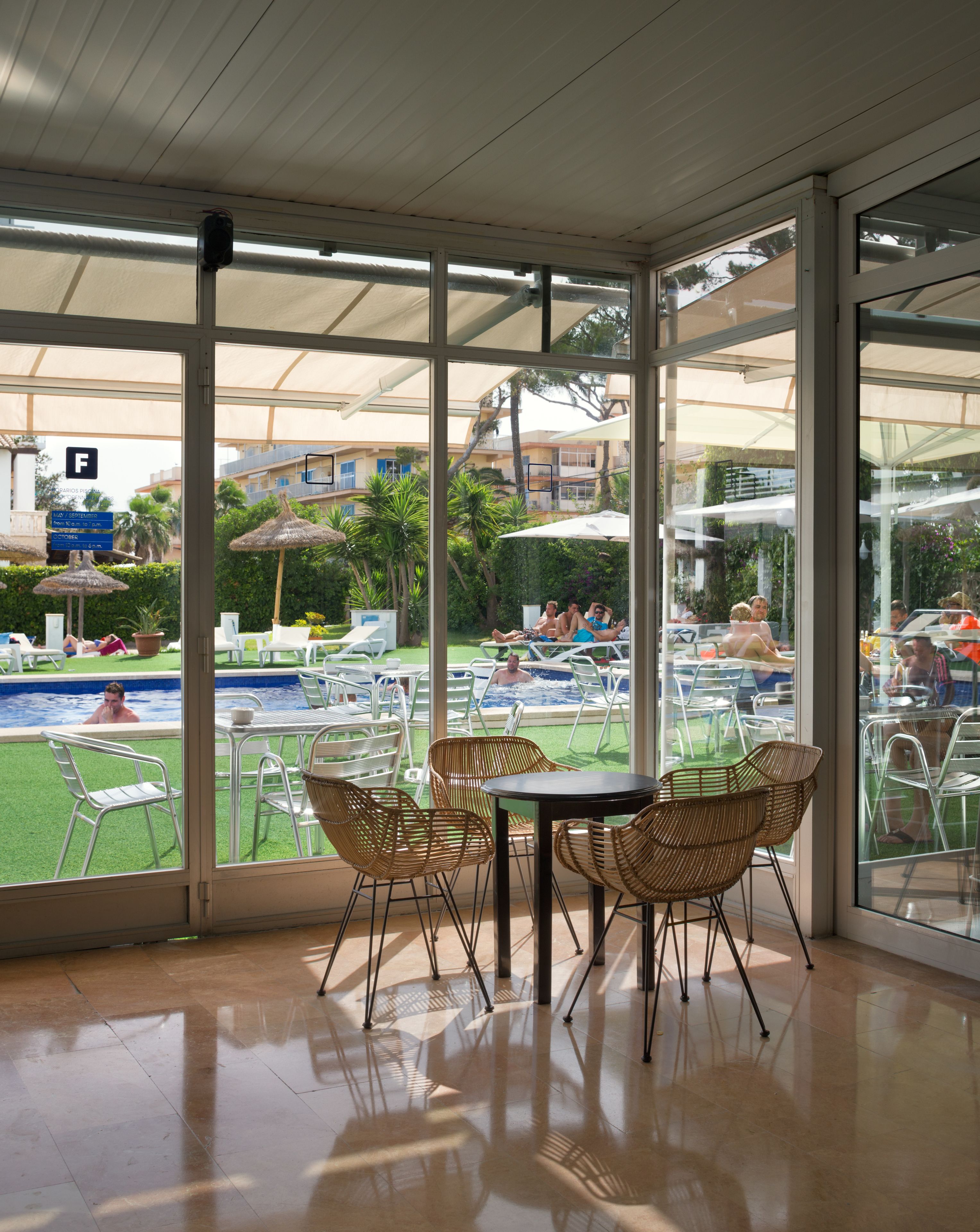 A glass-enclosed dining area with wicker chairs and a table, overlooking a pool and outdoor seating area.
