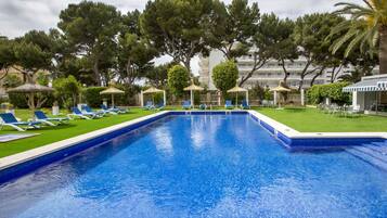 Una piscina con lettini e ombrelloni, immersa nel verde e con un edificio sullo sfondo.
