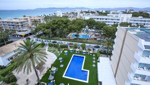 Ein Hotel mit Swimmingpool, umgeben von Liegestühlen und Sonnenschirmen, vor der Kulisse einer Küstenstadt.